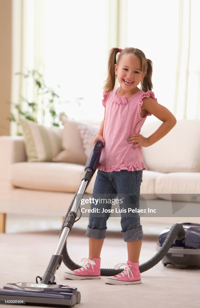 Grinning girl vacuuming living room floor