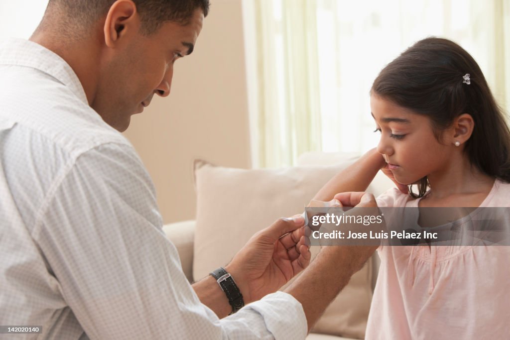 Father putting bandage on daughter's elbow
