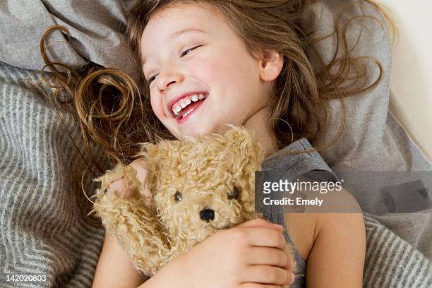 smiling girl holding teddy bear in bed - teddybär stock-fotos und bilder
