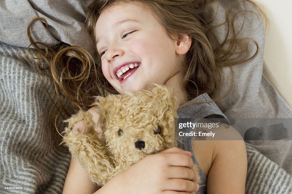 Smiling girl holding teddy bear in bed