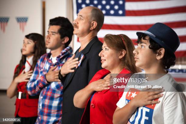 hispanic family pledging allegiance to the american flag - citizenship stockfoto's en -beelden