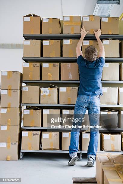 man filing cardboard boxes in storage - andar em bico de pés imagens e fotografias de stock