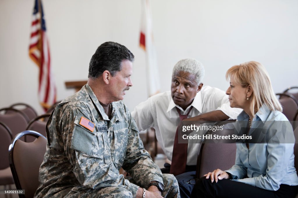 Soldier sitting in chair talking to business people