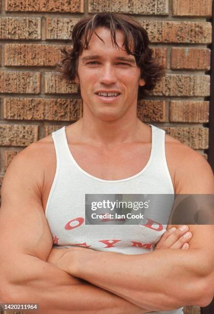 Portrait of Austrian bodybuilder Arnold Schwarzenegger, in a tank top as he poses, arms folded, against a brick wall, Santa Monica, California, 1977.