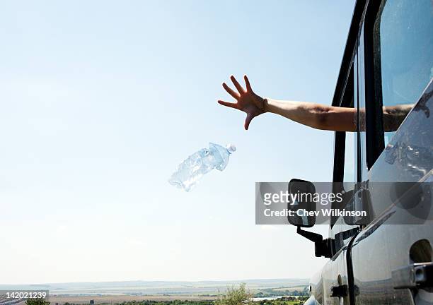woman throwing bottle out car window - throwing foto e immagini stock