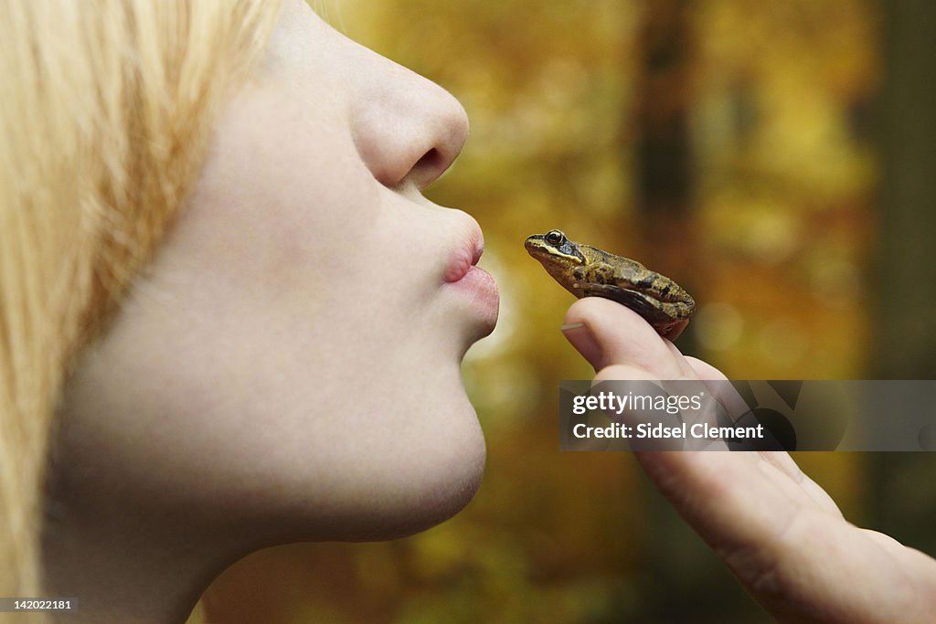 Girl kissing tiny frog in forest