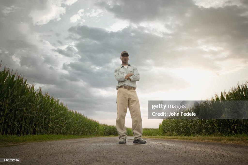 African American farmer standing on road through crops