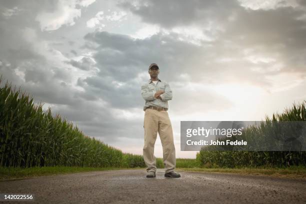 african american farmer standing on road through crops - low angle view imagens e fotografias de stock