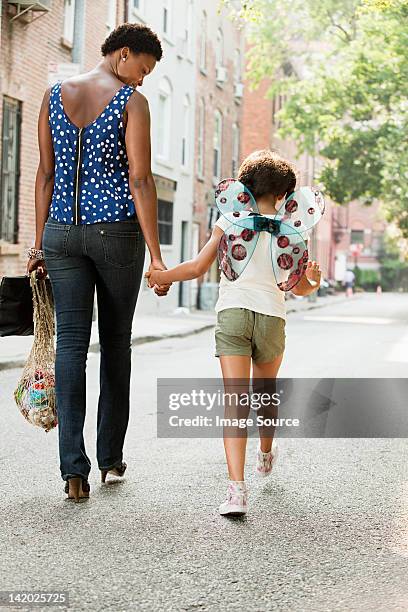 mother and daughter walking along street, rear view - wingwalking stock pictures, royalty-free photos & images