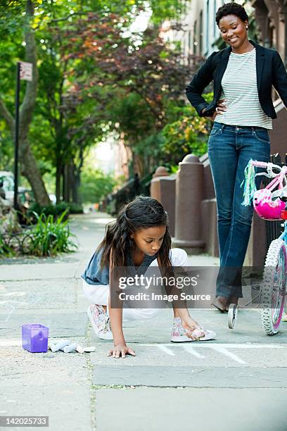 mother watching daughter draw on sidewalk - family chalk drawing stock pictures, royalty-free photos & images