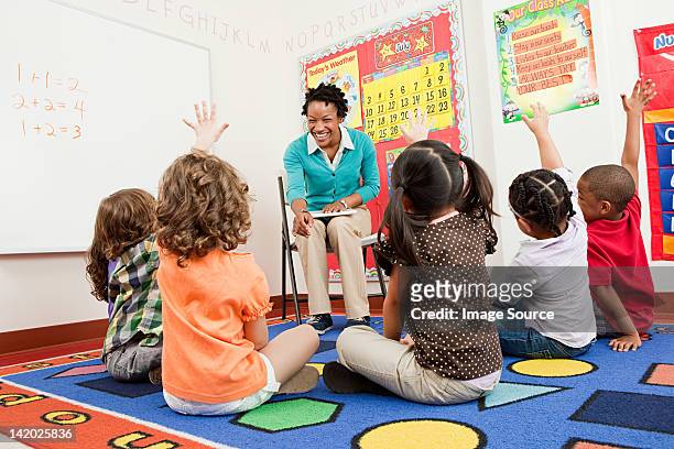 teacher and children sitting on floors with hands raised - boy sitting on floor stock pictures, royalty-free photos & images