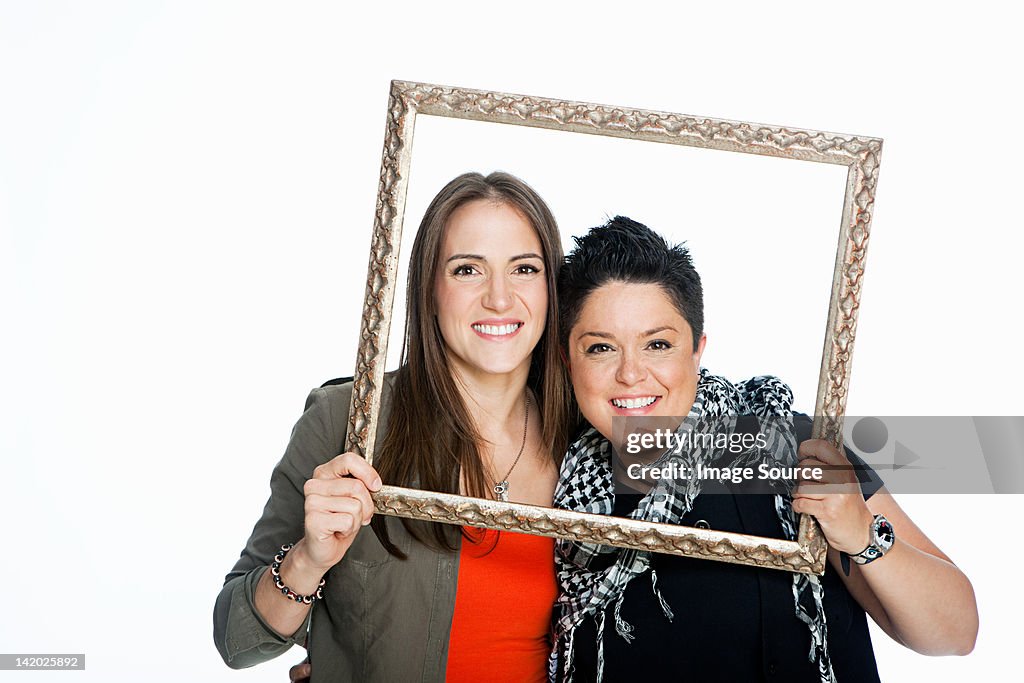 Lesbian couple holding picture frame against white background