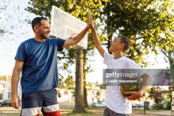 teenage boy high-fiving his father after they finished playing basketball together - parent and child stock pictures, royalty-free photos & images