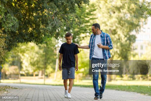 trauriger teenager beim spazierengehen mit seinem vater, der ihn tröstet - strict parent stock-fotos und bilder