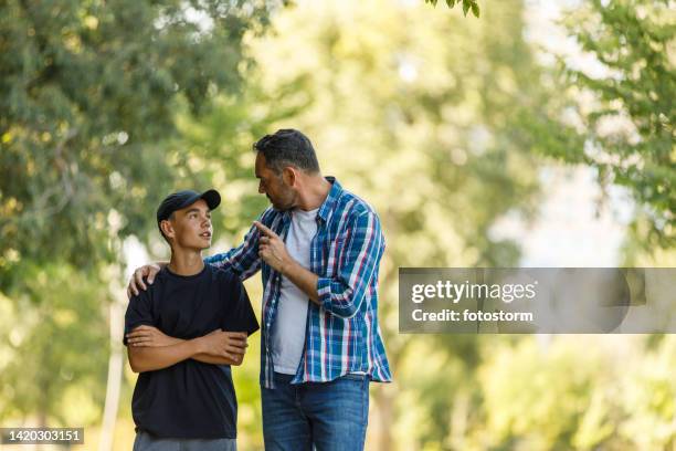 father embracing his son and telling him off while taking a walk at the park - scolding stock pictures, royalty-free photos & images