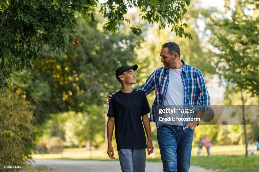 Front view of father and son walking embraced at the park, chatting and bonding