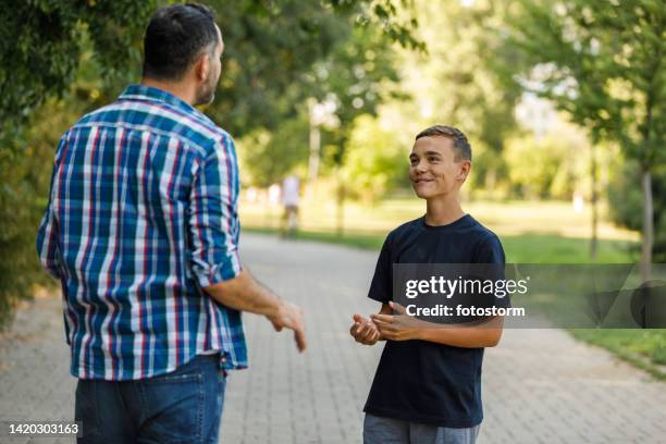 teenage boy and his father standing on the street, engaging in a discussion - teenager man mischievous stock pictures, royalty-free photos & images