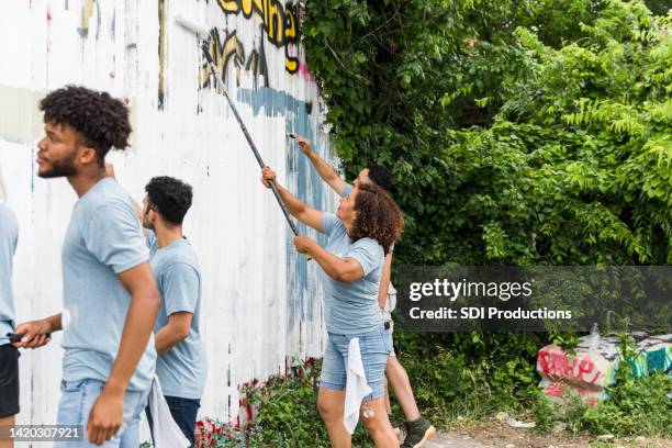 multiracial family works together to paint the graffiti wall - cleaning graffiti stock pictures, royalty-free photos & images