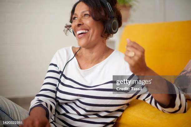 entspannen sie sich ältere frauen, die einen podcast, ein radio hören oder musik online streamen, während sie zu hause auf dem boden sitzen. reife afroamerikanerin, die lächelt und ein hörbuch in ihrem haus genießt - radio hören stock-fotos und bilder