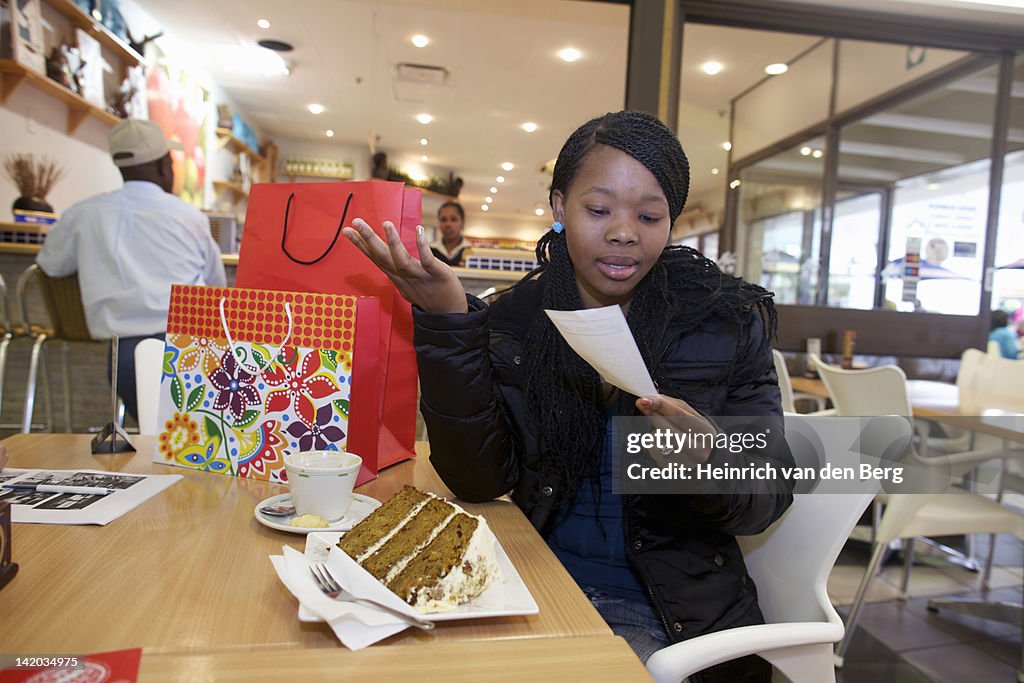 A young woman looking at the bill while sitting at a coffee shop. Pietermaritzburg, KwaZulu-Natal, South Africa