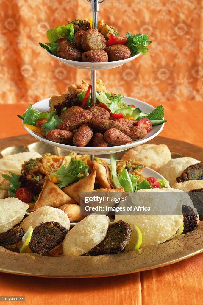 Indian cooking. A platter of snacks. Potato croquettes, samoosas, puri and patra served with lemon wedges and fresh salad greens