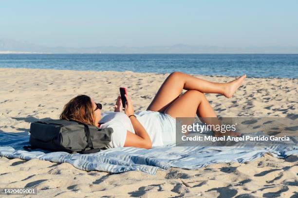 woman using mobile phone on the beach - girls sunbathing fotografías e imágenes de stock