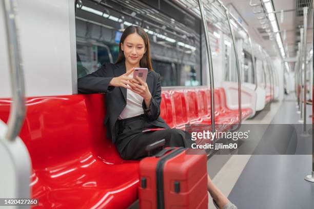 porträtfoto einer jungen asiatischen geschäftsfrau, die in einem s-bahn-zug und rotem gepäck reist und während der fahrt für eine geschäftsreise ein video auf ihrem smartphone anschaut - bahnreisender stock-fotos und bilder