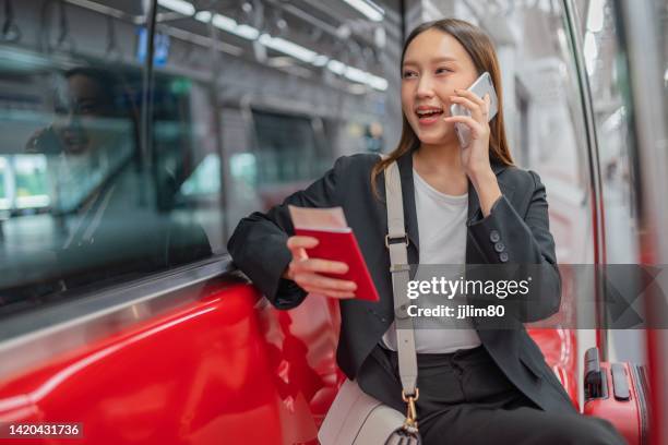 portrait photo of a young asian businesswoman lady traveling in a commuter rail train with her phone and red luggage going for a business travel - tourist talking on the phone stock pictures, royalty-free photos & images