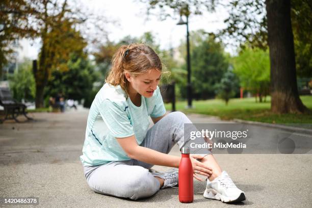 woman in pain sitting on the ground after twisting her ankle while jogging - twisted ankle stock pictures, royalty-free photos & images