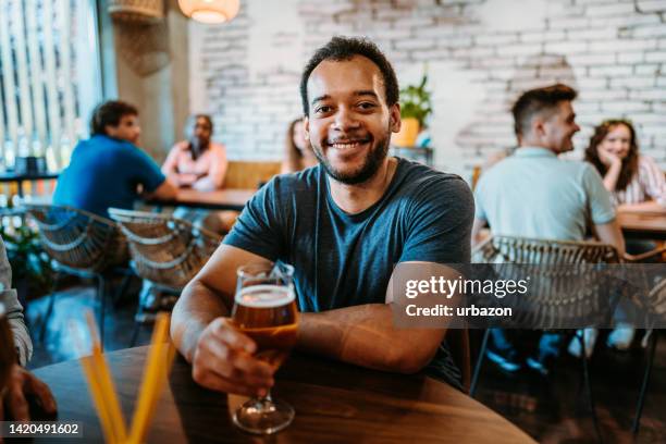 portrait of a young man drinking beer in a bar - lager stock pictures, royalty-free photos & images