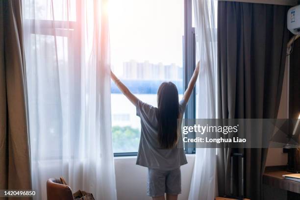 a young woman wakes up and pulls back the curtains - woman pulling hair back stock pictures, royalty-free photos & images