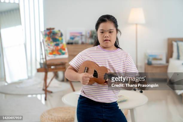 teenage girl with down's syndrome practicing ukelele with his mother at home - 旅行禁止 ストックフォトと画像