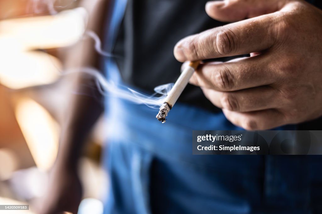 Detail of a man holding a smoking cigarette in his hand.
