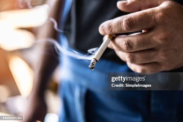 detail of a man holding a smoking cigarette in his hand. - stoppen met roken stockfoto's en -beelden