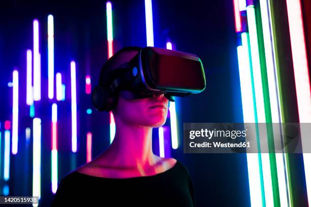 woman wearing virtual reality simulator near colorful illuminated lights - simulatore di realtà virtuale foto e immagini stock