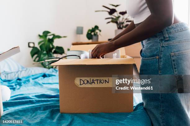 woman packing donation box on bed at home - declutter stockfoto's en -beelden