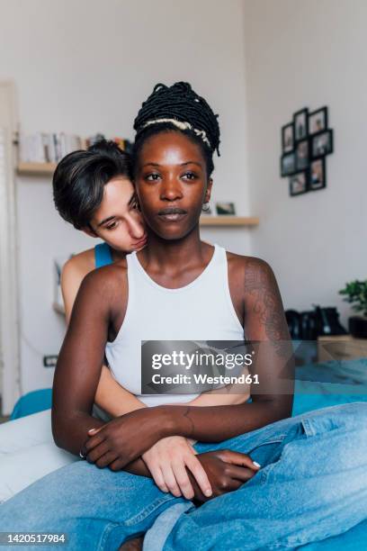 young woman embracing girlfriend from behind sitting on bed - lesbian bed stock pictures, royalty-free photos & images