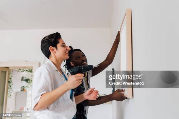 smiling woman adjusting picture frame by girlfriend at home - adjusting bildbanksfoton och bilder