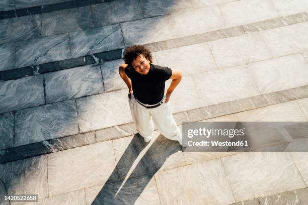 smiling young businesswoman standing with hands on hips - elevated view portrait stock pictures, royalty-free photos & images