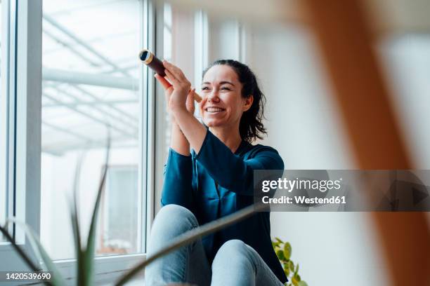 happy woman holding antique monocular sitting by window - fernrohr stock-fotos und bilder