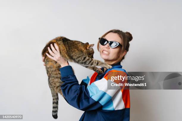 young woman with cat clenching teeth against white background - clenching teeth stock-fotos und bilder