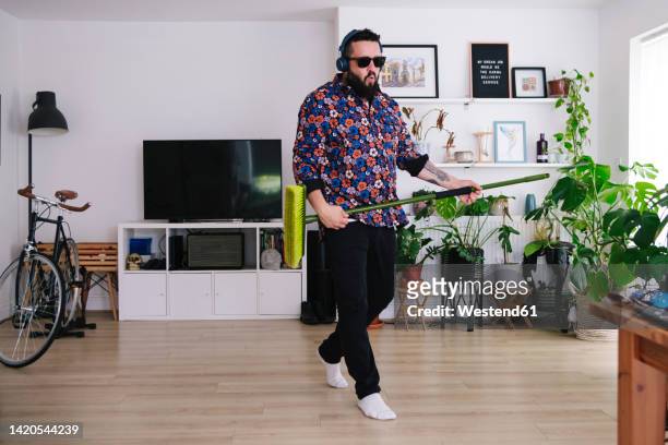 man wearing sunglasses dancing with broom at home - home cleaning stock-fotos und bilder