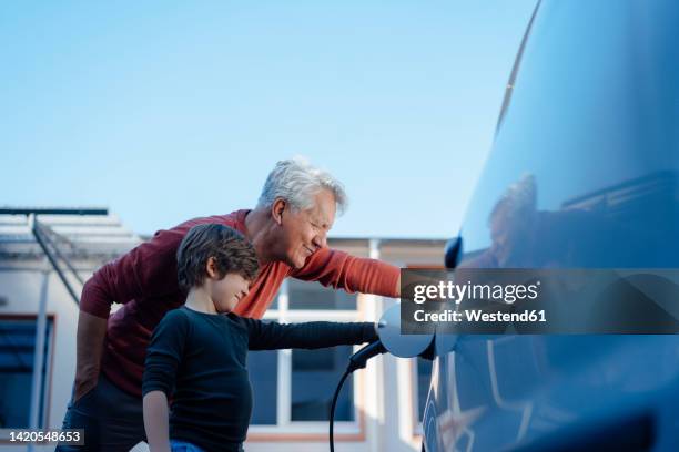 grandfather and grandson charging electric car - two generation family photos et images de collection