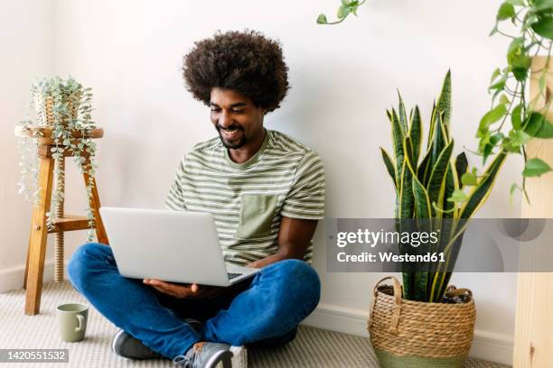 happy man using laptop sitting in front of wall at home - person in front of computer stock pictures, royalty-free photos & images