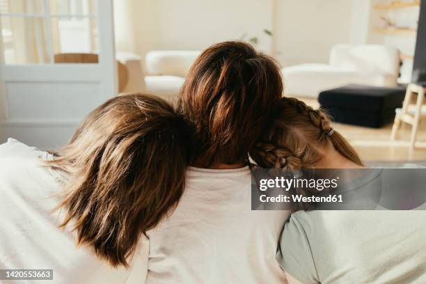 siblings leaning heads on mother's shoulder in living room at home - head on shoulder stock pictures, royalty-free photos & images