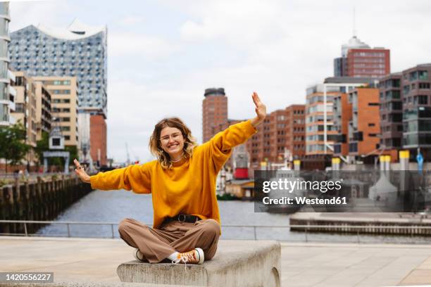 happy young woman with arms outstretched sitting on bench at elbphilharmonie - elbphilharmonie hamburg foto e immagini stock