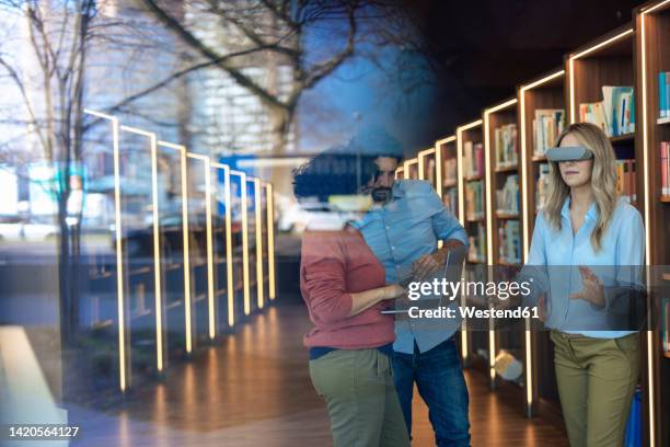 professors using laptop by colleague with smart glasses gesturing seen through glass - virtual library stock pictures, royalty-free photos & images