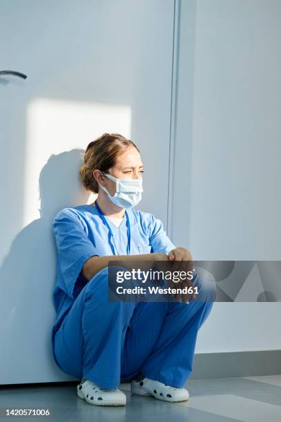 nurse wearing protective face mask squatting in front of wall at hospital - máscara quirúrgica fotografías e imágenes de stock