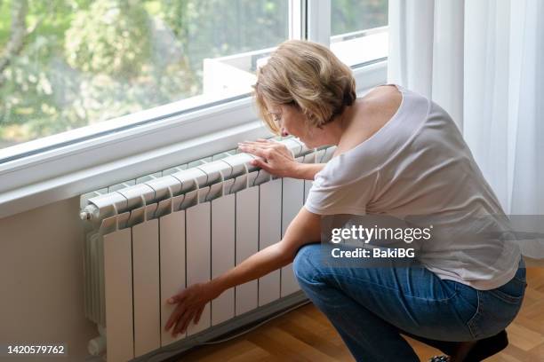 senior woman touching cold home radiator - electricity bill stock pictures, royalty-free photos & images