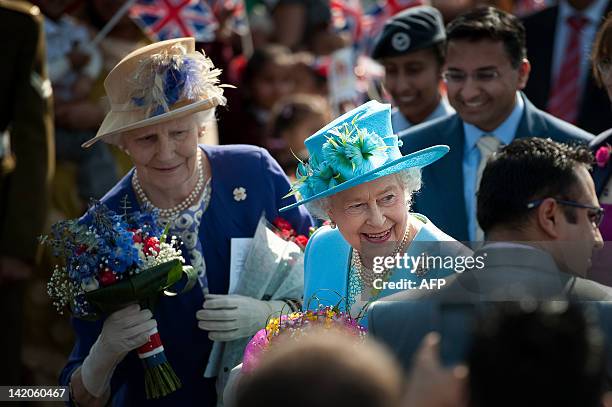 Britain's Queen Elizabeth II receives flowers from well-wishers followed by a lady-in-waiting as she leaves Krishna Avanti school in Harrow north...